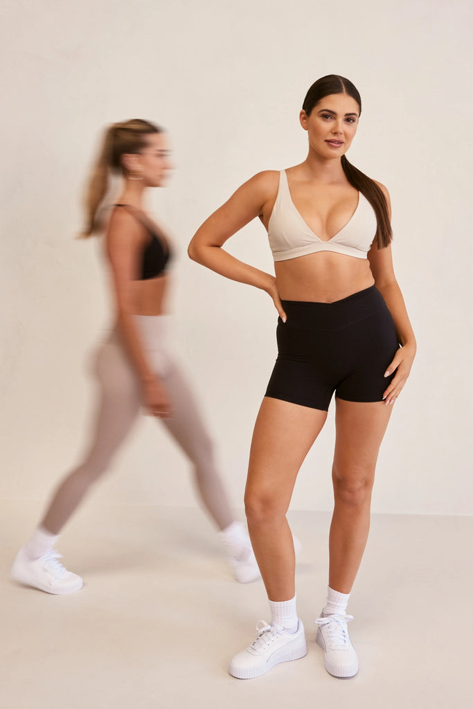 Model wearing YLAB Sports Bra and Shorts, with second model blurred and walking in the background